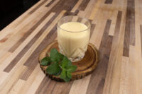 Glass of Czech Egg Liqueur – Czech Eggnog on a wood slice coaster with fresh mint on a striped wood table.