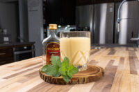 Glass of Czech Egg Liqueur – Czech Eggnog beside a Božkov Tuzemský bottle and fresh mint on a wood slice.