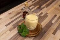 Glass of Czech Egg Liqueur – Czech Eggnog garnished with mint, small bottle behind it on wooden counter.