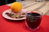 Glass of Czech Mulled Wine Svarak beside a pink plate with orange, cinnamon sticks, and cloves.