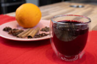 Glass of Czech Mulled Wine Svarak beside a plate of cloves, cinnamon sticks, and an orange.