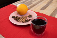 Glass of Czech Mulled Wine Svarak beside a pink plate with an orange, cinnamon sticks, and cloves.