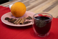 Glass of Czech Mulled Wine Svarak beside an orange, cinnamon, star anise and cloves on a red cloth