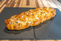 Braided Christmas Vánočka (Houska) loaf topped with sliced almonds on a dark slate board.