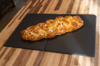 Braided Christmas Vánočka (Houska) loaf topped with sliced almonds on black slate.