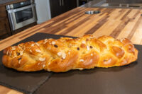 Braided Christmas Vánočka (Houska) loaf topped with sliced almonds on a dark slate board.