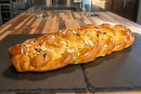 Braided Christmas Vánočka (Houska) topped with sliced almonds, resting on a dark slate board.