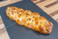 Braided Christmas Vánočka (Houska) loaf topped with sliced almonds on a dark slate board.