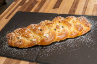 Braided Christmas Vánočka (Houska) loaf topped with sliced almonds and dusted with powdered sugar on a slate board.
