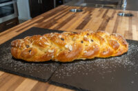 Braided Christmas Vánočka (Houska) loaf topped with sliced almonds and dusted with powdered sugar on slate boards.