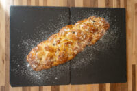 Braided Christmas Vánočka (Houska) loaf topped with sliced almonds and dusted with powdered sugar on a dark slate.