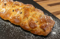 Braided Christmas Vánočka (Houska) loaf topped with sliced almonds and dusted with powdered sugar on a dark slate.