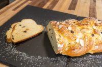 Braided Christmas Vánočka (Houska) with almonds and raisins, sliced, dusted with powdered sugar on slate