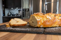 Braided Christmas Vánočka (Houska) loaf with almonds and raisins, one slice cut, on a slate board.