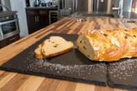 Braided Christmas Vánočka (Houska) with sliced almonds, two cut slices showing raisins, dusted with powdered sugar.