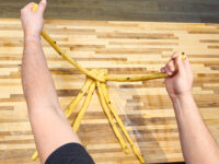Hands braid strands of dough for Christmas Vánočka (Houska) on a wooden board.