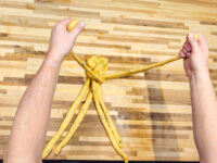 Hands braiding strands of dough into a knotted center while shaping Christmas Vánočka (Houska).