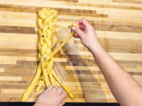 Hands braiding strands of pale dough for Christmas Vánočka (Houska) on a wooden cutting board