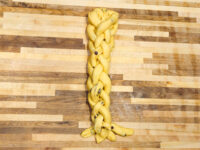 Braided raw dough studded with dark raisins, shaped for Christmas Vánočka (Houska) on a wooden board.