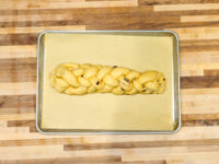 Braided Christmas Vánočka (Houska) dough with raisins, shaped and resting on parchment before baking