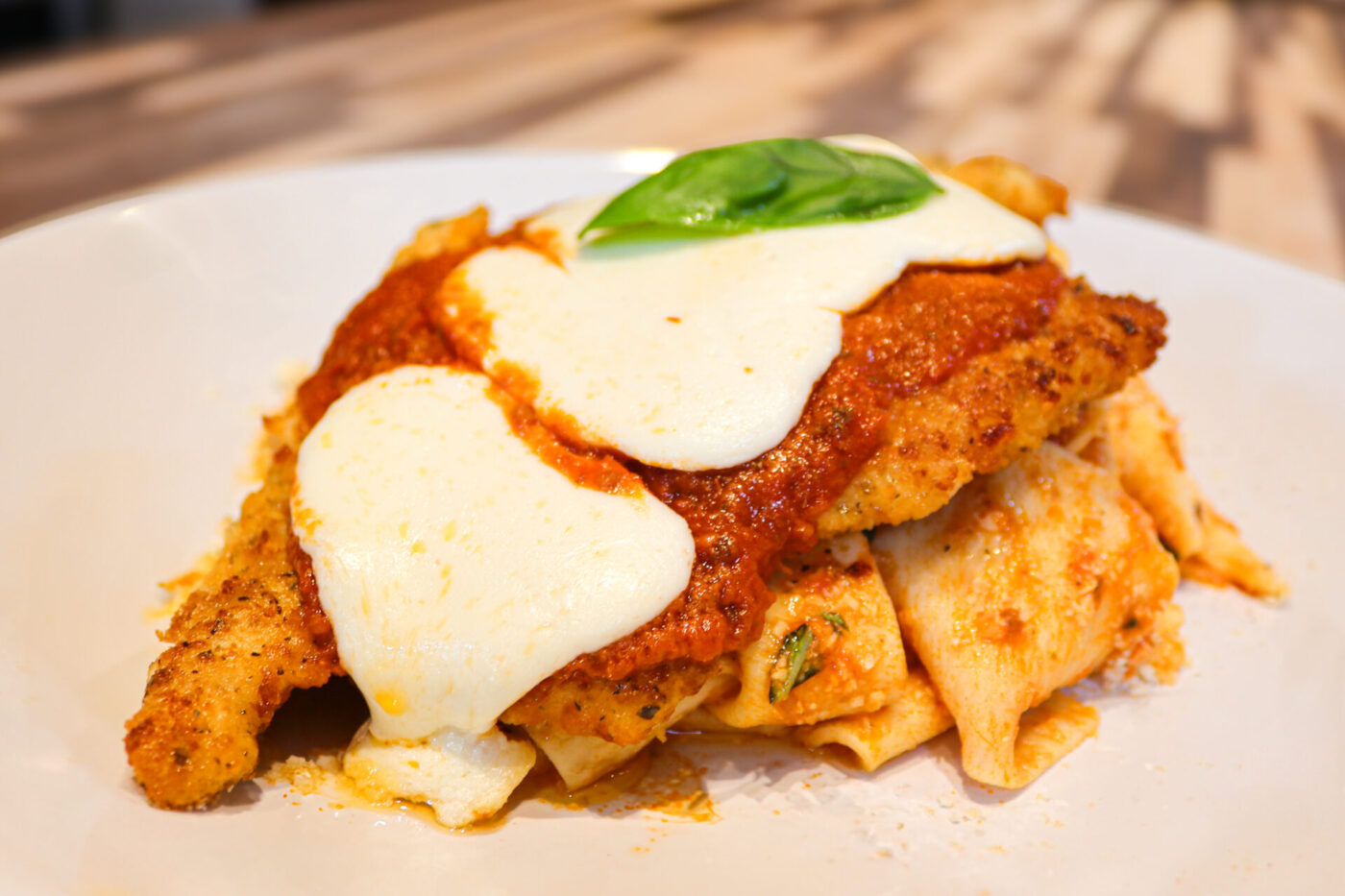 Breaded Chicken Parmesan topped with marinara, melted mozzarella, and basil, plated over pasta