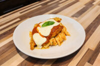 Chicken Parmesan cutlet with marinara and melted mozzarella over rigatoni, basil garnish, white plate.