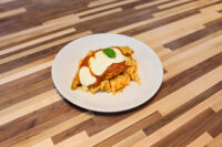 Chicken Parmesan cutlet topped with marinara sauce, melted cheese, and basil, served over pasta on a white plate.