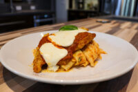 Chicken Parmesan with melted mozzarella and marinara sauce over rigatoni, garnished with basil.