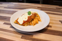 Chicken Parmesan topped with marinara and melted cheese, basil garnish, served with pasta on a white plate.