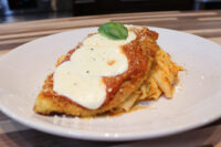 Breaded Chicken Parmesan cutlet with marinara and melted mozzarella over pasta, topped with basil.