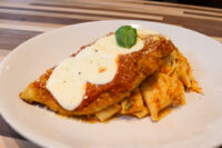 Breaded Chicken Parmesan topped with marinara sauce, melted cheese, and basil, plated over ribbon pasta.