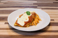 Breaded Chicken Parmesan topped with tomato sauce, melted cheese, and basil on a white plate.