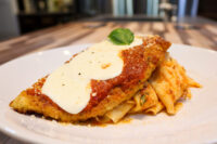 Chicken Parmesan cutlet with marinara and melted mozzarella, basil garnish, served with red-sauced pasta