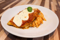 Breaded Chicken Parmesan topped with marinara, melted cheese, and basil, served over ribbon pasta on a white plate