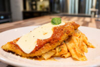 Breaded Chicken Parmesan topped with marinara and melted mozzarella, plated over ribbon pasta with a basil garnish.