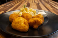 Crispy fried Fried Cauliflower Smažený Květák pieces on a black plate with diced potatoes and dip.
