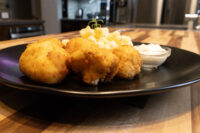 Three golden fried Smažený Květák cauliflower pieces on a black plate with diced fruit and dip