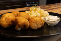 Breaded Fried Cauliflower Smažený Květák pieces on a black plate with potatoes and dip