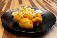 Breaded Fried Cauliflower Smažený Květák pieces on a black plate with diced potatoes and dip