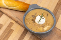 Bowl of Valašská Kyselica Soup topped with sour cream and a herb sprig, served with a bread roll