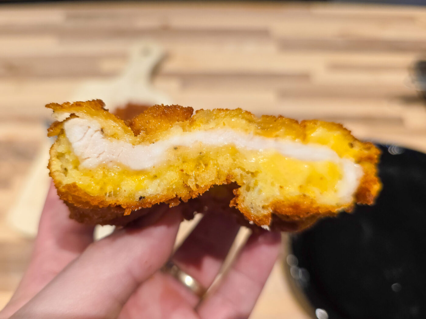 Bitten Cheese Battered Chicken Schnitzel Kuře v Sýrovem Těstíčku showing white meat and melted cheese, held in hand.