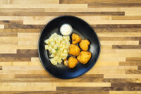 Fried Cauliflower Smažený Květák on a black plate with diced potatoes and white dip.