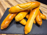 Stack of glossy golden Czech Rolls Rohliky, tapered and baked, piled on a dark slate board.