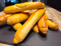 Stacked golden-brown Czech Rolls Rohliky piled on a dark slate board.