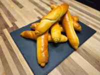 Pile of glossy, twisted Czech Rolls Rohliky on a dark slate board atop a wooden table.