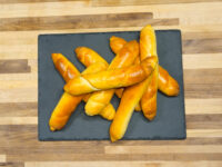 Golden-brown Czech Rolls Rohliky piled on a dark slate board on a wooden table.