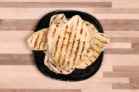 Garlic Naan Bread with charred grill stripes stacked on a black plate on a wooden table