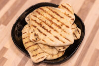 Stack of grilled Garlic Naan Bread with char marks in a black dish on a wooden table