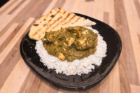 A grilled naan bread wedge served alongside spinach curry and rice on a black plate.