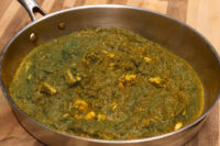 Stainless steel pan of Spinach Palak Paneer with pale paneer chunks in thick green curry.
